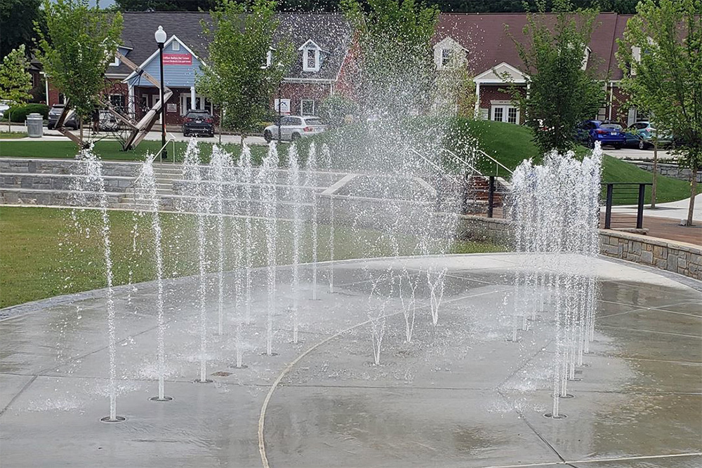 A large splash pad outside with multiple fountain jets in a residential community.