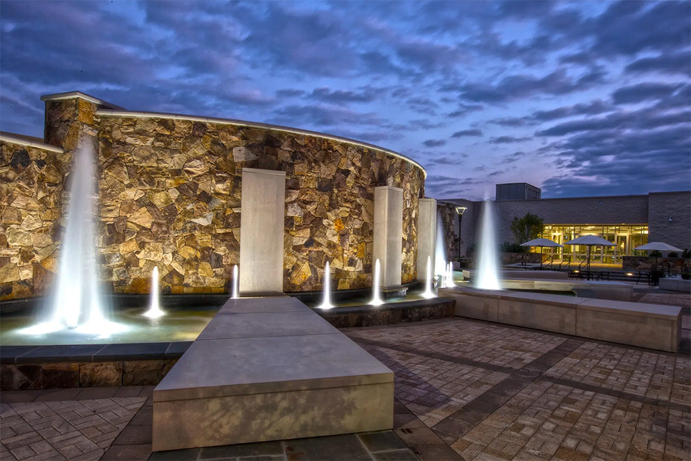 A large stone fountain outside with several smaller fountains on a brick plaza.
