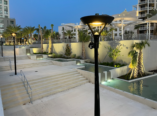 Terraced concrete water feature with cascading pools and uplit palm trees at dusk in a mixed-use urban plaza.